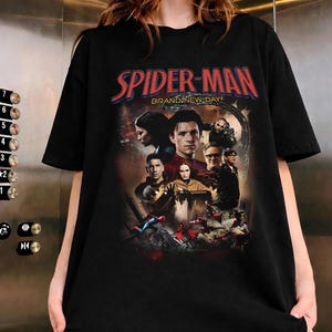 Op de afbeelding: Zwart T-shirt met een Spider-Man filmgrafiek. Het ontwerp bevat de rode tekst "SPIDER-MAN" en de zin "BRAND-NEW DAY". De afbeelding toont verschillende personages uit de film.