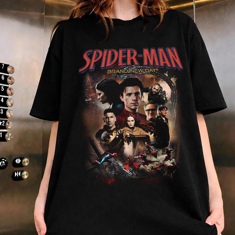 Op de afbeelding: Zwart T-shirt met een Spider-Man filmgrafiek. Het ontwerp bevat de rode tekst "SPIDER-MAN" en de zin "BRAND-NEW DAY". De afbeelding toont verschillende personages uit de film.