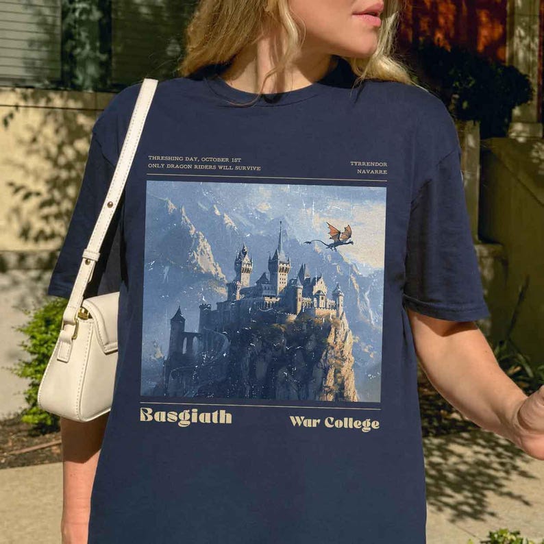 May include: Navy blue t-shirt featuring a fantasy landscape with a castle, mountains, and a dragon. The text on the shirt reads "THRESHING DAY, OCTOBER 1ST ONLY DRAGON RIDERS WILL SURVIVE" and "Basgiath War College".