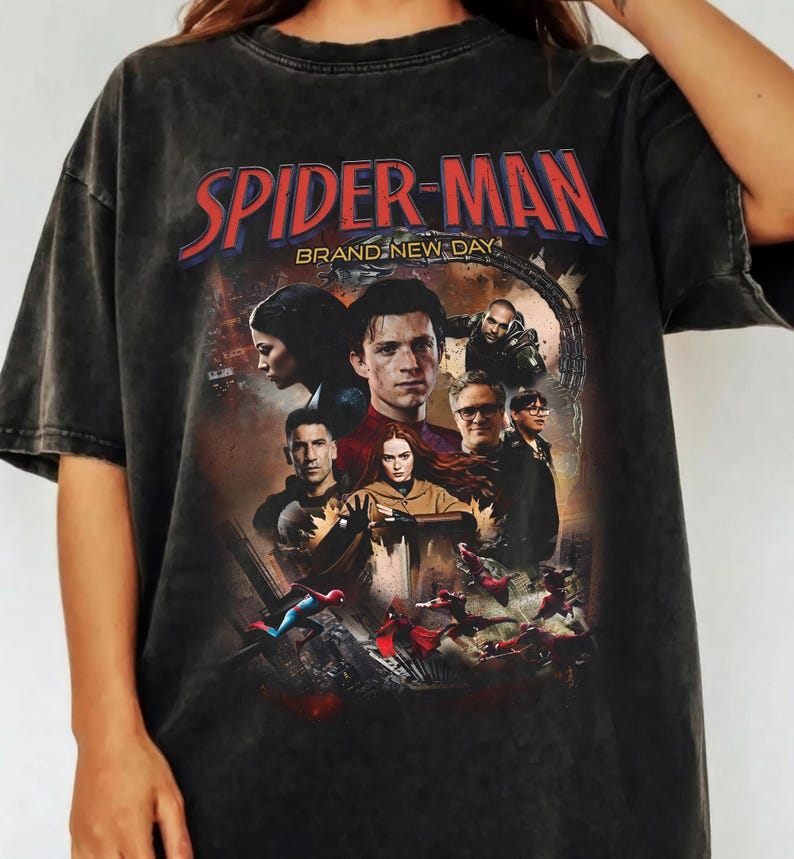 Op de afbeelding: Donkergrijs T-shirt met een Spider-Man-afbeelding en de tekst "SPIDER-MAN BRAND NEW DAY". De afbeelding bevat afbeeldingen van personages uit de film. Het shirt heeft een vintage, versleten uitstraling.