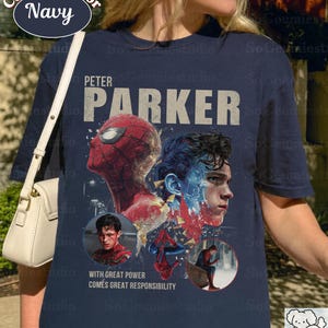 May include: A navy blue short-sleeve t-shirt featuring a graphic print of Peter Parker and Spider-Man. The design includes the text "PETER PARKER" and "WITH GREAT POWER COMES GREAT RESPONSIBILITY," along with two circular insets showing the character.