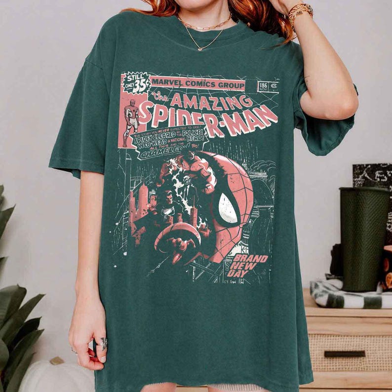 Puede incluir: Camiseta verde oscuro con un dise&ntilde;o de portada de c&oacute;mic vintage. El gr&aacute;fico incluye el texto "The Amazing Spider-Man" y una ilustraci&oacute;n de la cara de Spider-Man. La camiseta tiene un aspecto cl&aacute;sico y ligeramente descolorido.