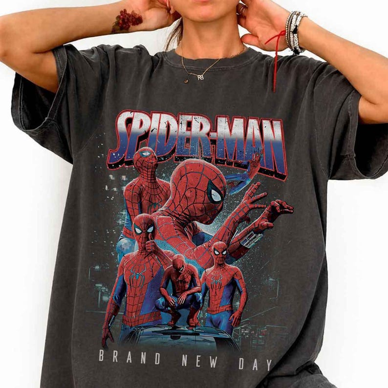 May include: Charcoal grey t-shirt with a Spider-Man graphic. The design shows Spider-Man in action poses, with the text "SPIDER-MAN" in red and blue. The words "BRAND NEW DAY" are printed below. The shirt has a faded, vintage appearance.