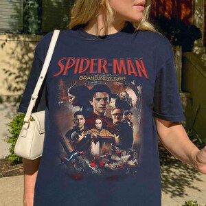 Op de afbeelding: Marineblauw T-shirt met een Spider-Man-afbeelding en de tekst "SPIDER-MAN BRAND NEW DAY" in het rood. De afbeelding bevat afbeeldingen van personages uit de film. Het shirt heeft korte mouwen en een ronde hals.