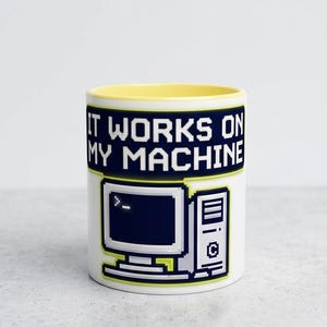 May include: White ceramic mug with a yellow interior. The mug features a pixelated design of a computer and the text "IT WORKS ON MY MACHINE" in white letters on a dark blue background.