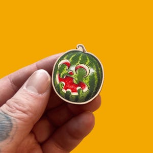 May include: A green watermelon with a carved out smiling face. The watermelon is painted with red and white details.