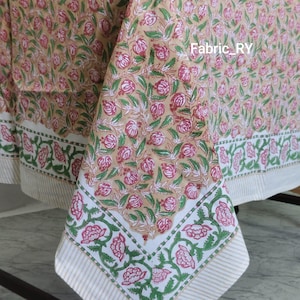 Puede incluir: Un mantel beige con un estampado floral de flores rosas y hojas verdes. El borde presenta una banda blanca con flores rosas y hojas verdes, y un patrón de rayas. El texto "Fabric_RY" es visible.