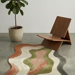 May include: A wavy, multi-colored rug with a modern design. The rug features layers of colors including shades of brown, green, pink, and white. A wooden chair and a potted plant are in the background. The rug's dimensions are approximately 60 inches by 40 inches.