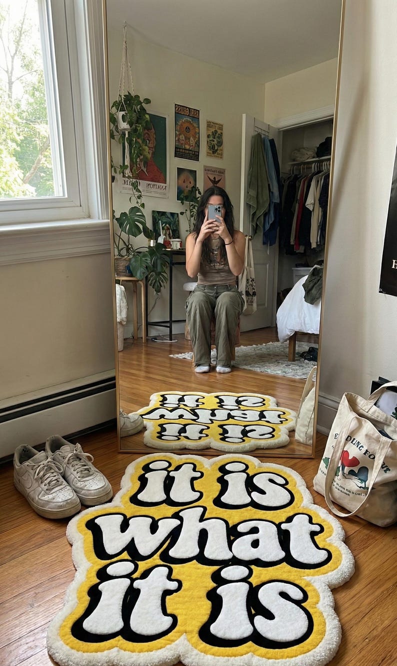 Hand-tufted rectangular doormat with bright yellow “It Is What It Is” lettering, featuring a soft, textured pile and sturdy backing; ideal for welcoming guests while adding a bold, humorous statement to home decor.