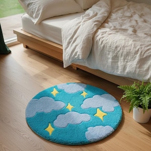 May include: A round, turquoise rug with a sky design featuring fluffy gray clouds and yellow stars. The rug is placed on a wooden floor near a bed with white bedding. A small potted fern is visible.