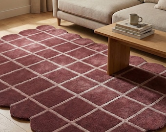May include: A burgundy-colored area rug with a geometric diamond pattern. The rug has a scalloped edge and is placed on a hardwood floor. A beige sofa and wooden coffee table are in the background.