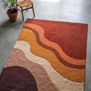 Può includere: Un tappeto rettangolare con un design ondulato nei toni del rosso, arancione, beige e marrone. Una sedia di legno e una pianta in vaso sono sullo sfondo. Le dimensioni del tappeto non sono visibili.