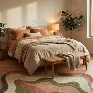 May include: A bedroom scene featuring a bed with terracotta-colored bedding and a neutral-toned throw. A wooden bench sits at the foot of the bed, and a multi-colored, wavy rug in shades of green, pink, and gray lies on the floor. A lamp and plants add to the cozy atmosphere.