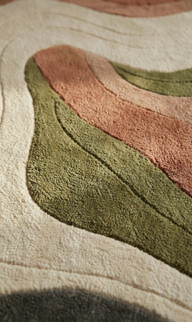 May include: Close-up of a textured rug with a wavy design. The rug features stripes of beige, olive green, and muted coral colors. The soft, plush texture is visible, suggesting a comfortable floor covering.