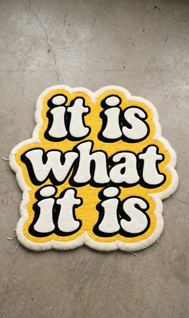 Soft and durable tufted mat displaying the phrase “It Is What It Is” in yellow glow lettering, designed for indoor use in entryways or living rooms; the textured surface provides comfort while enhancing a modern, personalized decor style.