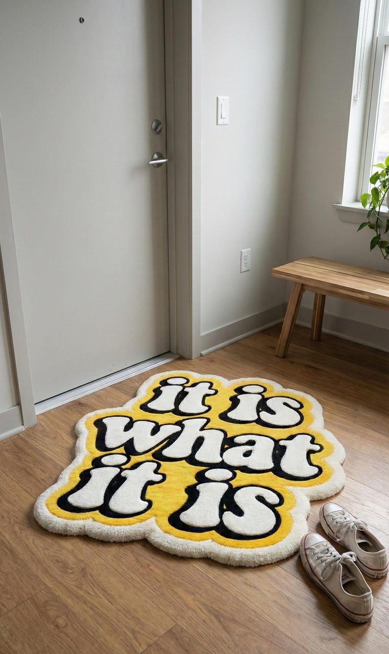 Personalized yellow-lettered “It Is What It Is” tufted mat with a textured, plush surface and rectangular shape; suitable for indoor entryways, living rooms, or decorative floor accents that combine style with function.
