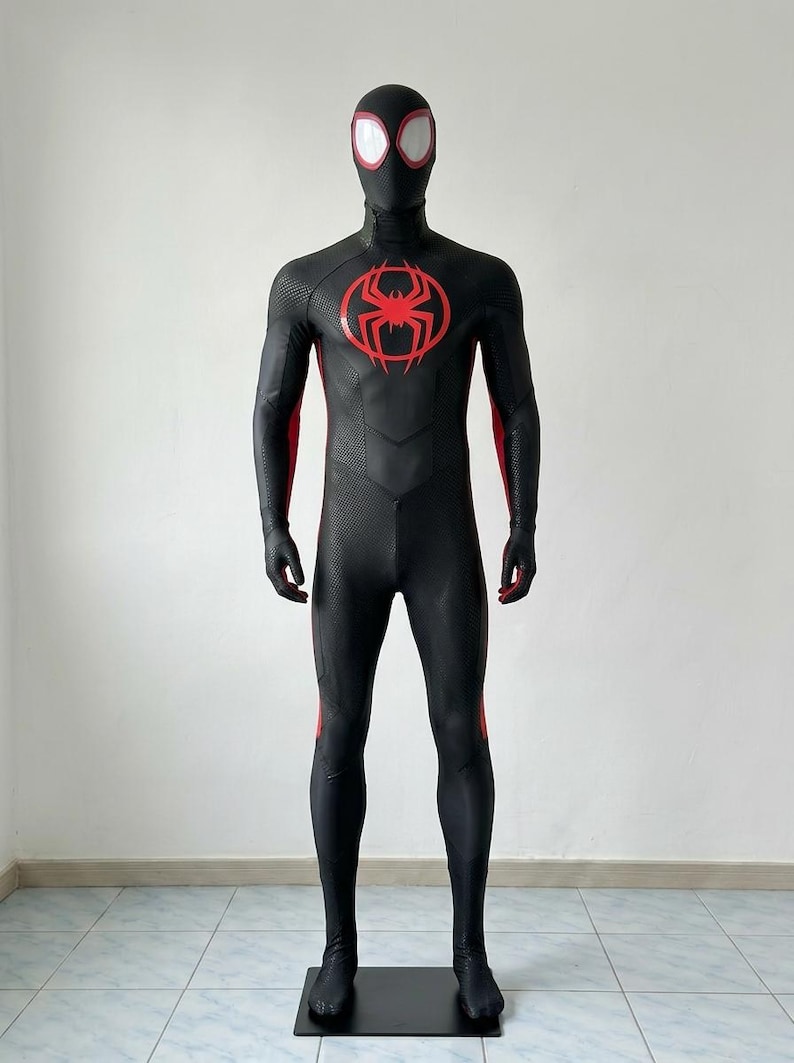 May include: A full-body black spandex suit featuring a red spider emblem on the chest, a matching black mask with white eye lenses, and red accents along the sides of the arms and legs. The fabric has a textured pattern throughout the torso.