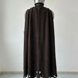 May include: A full-length dark brown textured cape worn over a metallic silver helmet and armor set. The cape features a distressed, frayed hemline with visible holes and uneven edges, draped over the shoulders and extending down to the boots.
