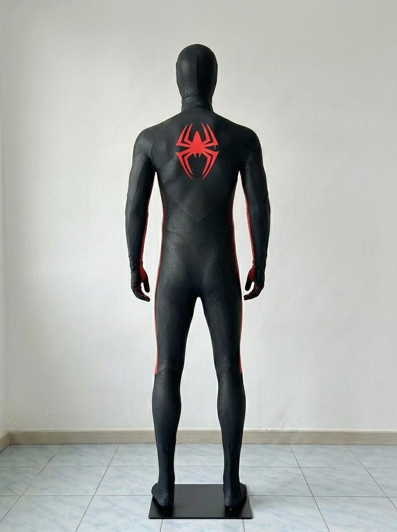 May include: A full-body black spandex suit featuring a textured honeycomb pattern throughout. The back displays a large, stylized red spider emblem centered between the shoulder blades, with red vertical stripes running down the sides of the legs.