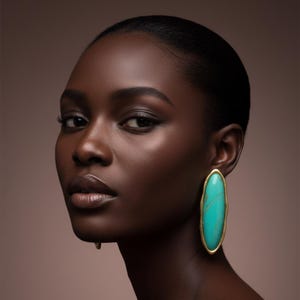 May include: An oval-shaped earring featuring a smooth, bright turquoise stone set within a textured gold-toned metal frame. The earring has a long, vertical orientation and a polished finish, showcasing a distinct marbled pattern on the stone surface.