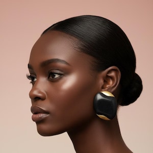 May include: A large, oval-shaped earring featuring a smooth, matte black center section contrasted by textured, metallic gold accents at the top and bottom edges. The piece has a bold, rounded silhouette and a secure, flush-fitting design.