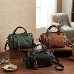 May include: Three barrel-shaped handbags in dark green, brown, and black. Each bag features a top handle, a detachable shoulder strap, a front pocket, and a decorative metal chain with a matching tassel charm attached to the handle hardware.