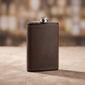 May include: A rectangular pocket flask wrapped in dark brown textured material with visible stitching along the edges. The flask features a black top section and a metallic silver screw-top cap with a hinged arm attached to the neck of the container.