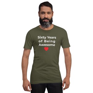 May include: Olive green short-sleeve t-shirt with the text "Sixty Years of Being Awesome" in white, and a red heart graphic. The t-shirt is made of a soft material.