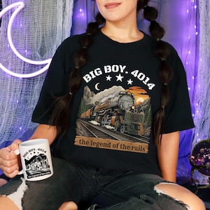 May include: Black t-shirt with a train graphic and the text "BIG BOY. 4014" above the image of a steam train. A white mug with the same train graphic and text is also visible. The phrase "the legend of the rails" is printed on both items.