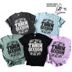 Peut inclure: Cinq t-shirts de couleurs variées : charbon, bleu clair, vert sauge, noir et lavande. Chaque t-shirt affiche le texte "DON'T TEST ME TRAIN STATION IN MY GPS" en blanc gras. Les t-shirts sont à manches courtes et de style décontracté.