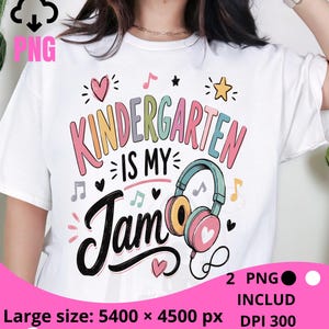 Peut inclure: Un t-shirt blanc avec un motif coloré portant l'inscription "KINDERGARTEN IS MY Jam" en polices rose, bleue et noire. Le design comprend des illustrations de casque audio rose et jaune, de petits cœurs, d'étoiles et de notes de musique.
