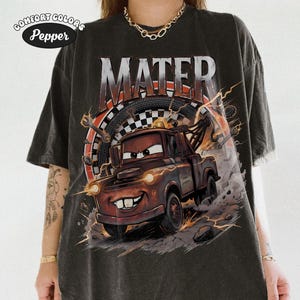 May include: Dark gray t-shirt featuring a cartoon image of Mater from the movie Cars. The word "MATER" is printed above the character. The shirt has a distressed look and the Comfort Colors Pepper logo is in the upper left corner.