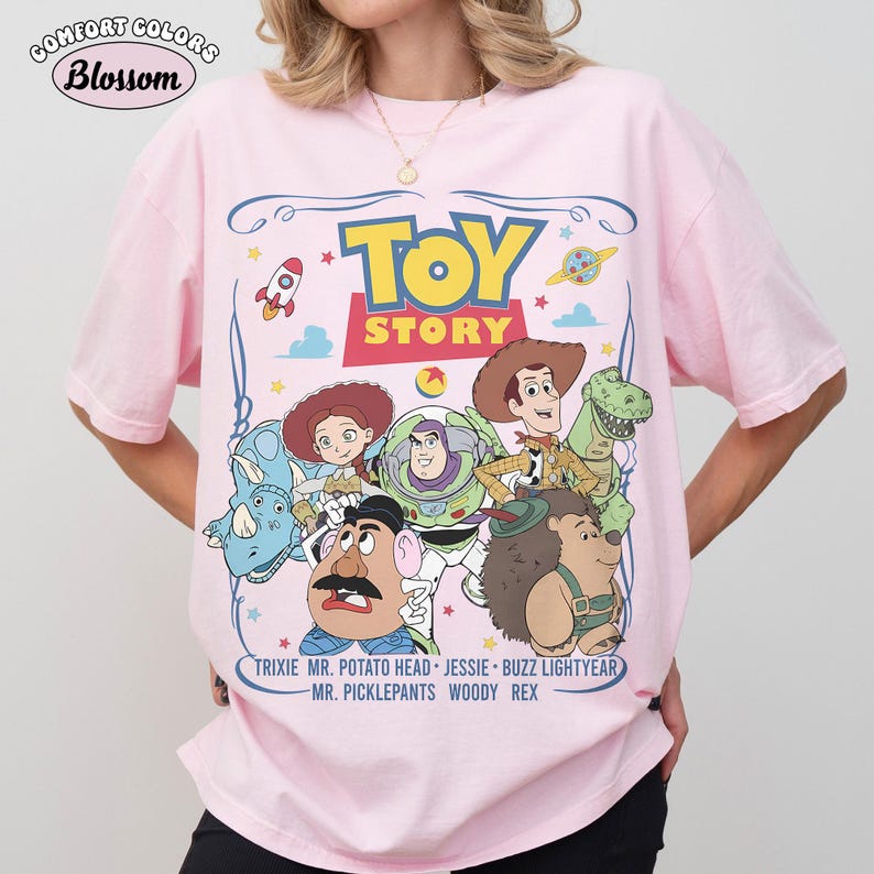May include: Pink Comfort Colors t-shirt featuring the Toy Story movie characters. The design includes Woody, Buzz Lightyear, Jessie, Mr. Potato Head, Rex, and Mr. Pricklepants. The shirt also has the text "Toy Story" and character names.