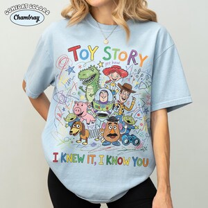 Puede incluir: Una camiseta azul claro con un gr&aacute;fico colorido de los personajes de Toy Story, incluyendo a Woody, Buzz Lightyear, Jessie, Rex, Hamm, Slinky Dog, Mr. Potato Head y los Aliens. El dise&ntilde;o incluye garabatos tipo cray&oacute;n y el texto "TOY STORY" y "I KNEW IT, I KNOW YOU".