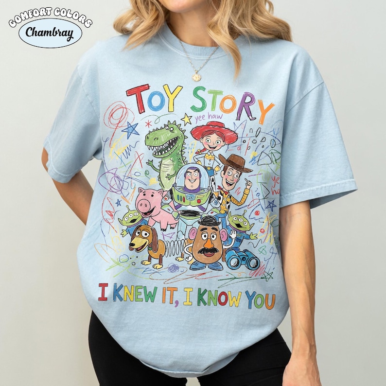Puede incluir: Una camiseta azul claro con un gr&aacute;fico colorido de los personajes de Toy Story, incluyendo a Woody, Buzz Lightyear, Jessie, Rex, Hamm, Slinky Dog, Mr. Potato Head y los Aliens. El dise&ntilde;o incluye garabatos tipo cray&oacute;n y el texto "TOY STORY" y "I KNEW IT, I KNOW YOU".
