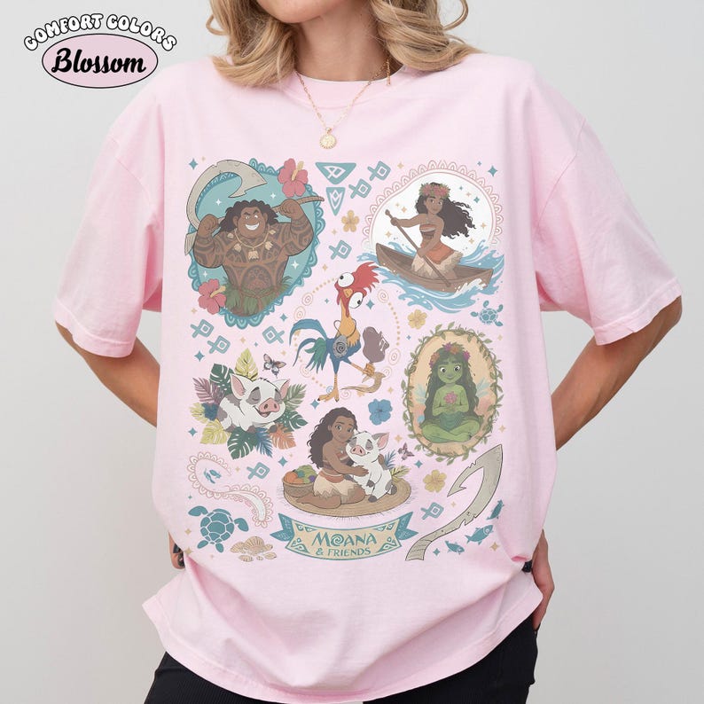 May include: Pink Comfort Colors t-shirt featuring a colorful graphic of characters from the animated film Moana. The design includes illustrations of Maui, Moana, Pua, Hei Hei, and other elements from the movie. The text "Moana & Friends" is also included.