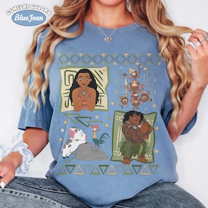 May include: A blue t-shirt featuring a graphic print of characters from the movie Moana, including Moana, Maui, Pua the pig, Heihei the rooster, and Kakamora. The design includes geometric patterns and the text Comfort Colors Blue Jean.