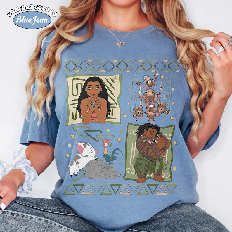 May include: A blue t-shirt featuring a graphic print of characters from the movie Moana, including Moana, Maui, Pua the pig, Heihei the rooster, and Kakamora. The design includes geometric patterns and the text Comfort Colors Blue Jean.