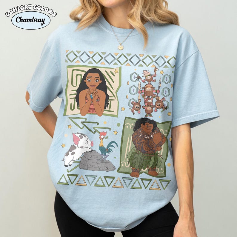 May include: A light blue short-sleeve t-shirt featuring a graphic print of characters from the movie Moana, including Moana, Maui, Pua, Heihei, and the Kakamora. The design includes geometric patterns and small stars on a light blue fabric.