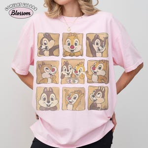 May include: A pale pink t-shirt with a grid of Chip and Dale cartoon character images. The shirt has the words "Comfort Colors" and "Blossom" printed on the top left corner. The t-shirt has a relaxed fit.