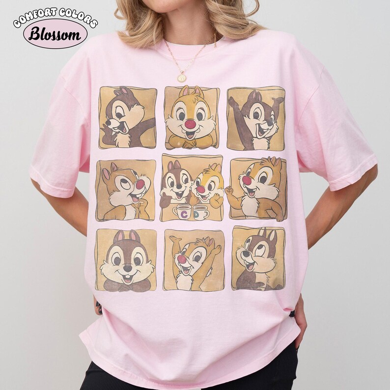 May include: A pale pink t-shirt with a grid of Chip and Dale cartoon character images. The shirt has the words "Comfort Colors" and "Blossom" printed on the top left corner. The t-shirt has a relaxed fit.