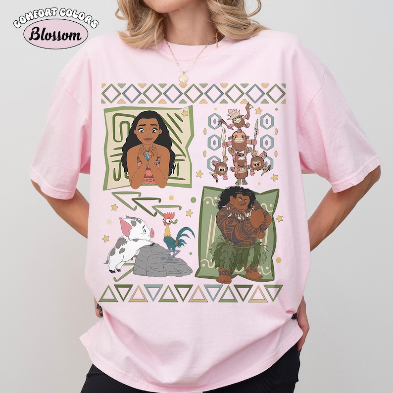 May include: A light pink short-sleeve t-shirt featuring a graphic print of characters from the movie Moana, including Moana, Maui, Pua, Heihei, and the Kakamora. The design includes geometric patterns, stars, and the text Comfort Colors Blossom.