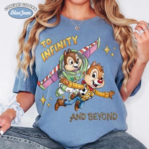 May include: A light blue Comfort Colors t-shirt featuring Chip and Dale as Buzz Lightyear and Woody, with the text "TO INFINITY AND BEYOND". The design includes stars and a spaceship wing.