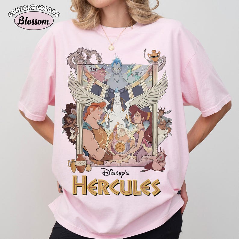 May include: Pink Comfort Colors t-shirt featuring a graphic from Disney's Hercules. The design includes Hercules, Megara, and other characters, with the text "Disney's Hercules" in gold. The shirt also has the text "Blossom" in a circle.