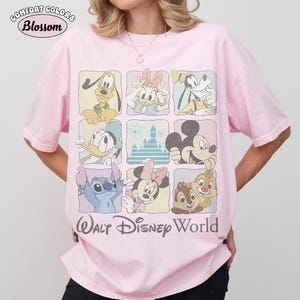 Op de afbeelding: Een lichtroze T-shirt met korte mouwen voorzien van een raster van negen vierkanten met illustraties van Disney-figuren waaronder Pluto, Katrien Duck, Goofy, Donald Duck, een kasteel, Mickey Mouse, Stitch, Minnie Mouse en Knabbel en Babbel, met Walt Disney World tekst.