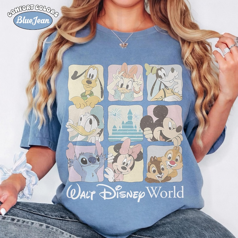 Op de afbeelding: Een blauw t-shirt met korte mouwen voorzien van een raster van negen vierkanten met illustraties van Disney-figuren zoals Pluto, Katrien Duck, Goofy, Donald Duck, een kasteel, Mickey Mouse, Stitch, Minnie Mouse en Knabbel en Babbel, met de tekst Walt Disney World.