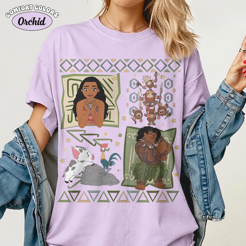 May include: A light purple short-sleeve t-shirt featuring a graphic print of characters from the movie Moana, including Moana, Maui, Pua, Heihei, and the Kakamora. The design includes geometric patterns and the text Comfort Colors Orchid.