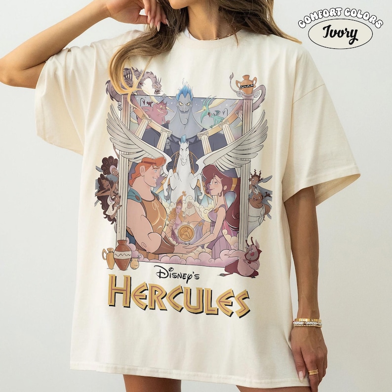 May include: Ivory-colored Comfort Colors t-shirt featuring a graphic from Disney's Hercules. The design includes Hercules, Megara, Pegasus, and other characters. The shirt has a relaxed fit.