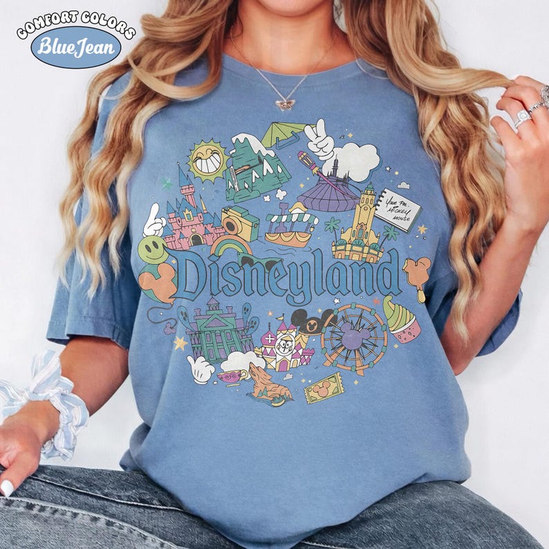 May include: Blue Comfort Colors t-shirt with a Disneyland graphic. The graphic features various park icons, including a castle, Matterhorn, and Mickey Mouse. The text "Disneyland" is prominently displayed in a whimsical font.
