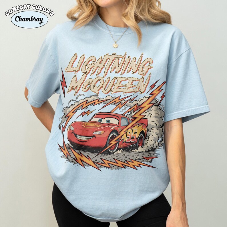 May include: Light blue t-shirt featuring a graphic of Lightning McQueen from the Cars movie. The design includes the text "LIGHTNING McQUEEN" in a stylized font, with lightning bolts and racing details. The number 95 is visible on the car.